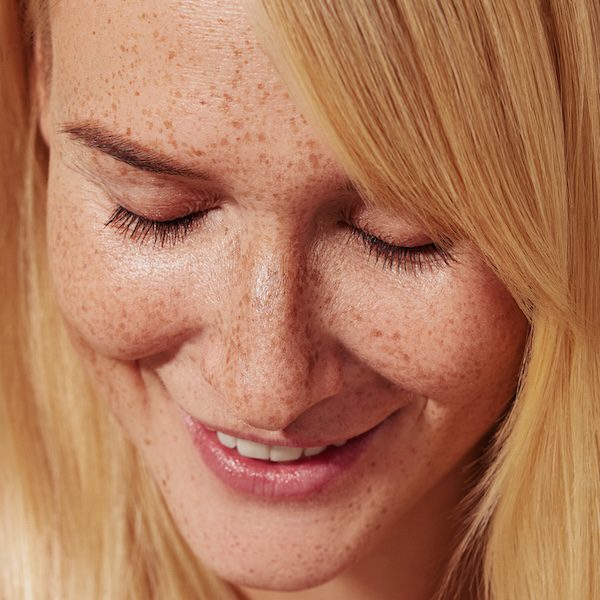 Close-up of smiling blond female with freckles looking down. Highly detailed close-up shot of a young female with smooth freckled skin.