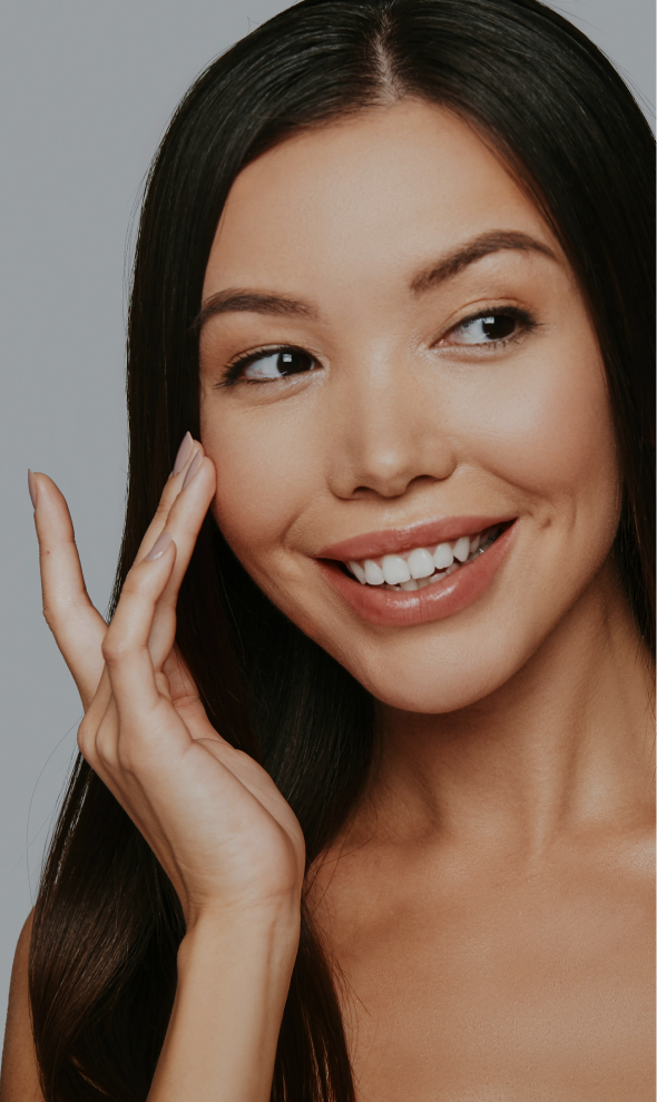 A smiling woman with bright, even skin, her fingertips at her cheek
